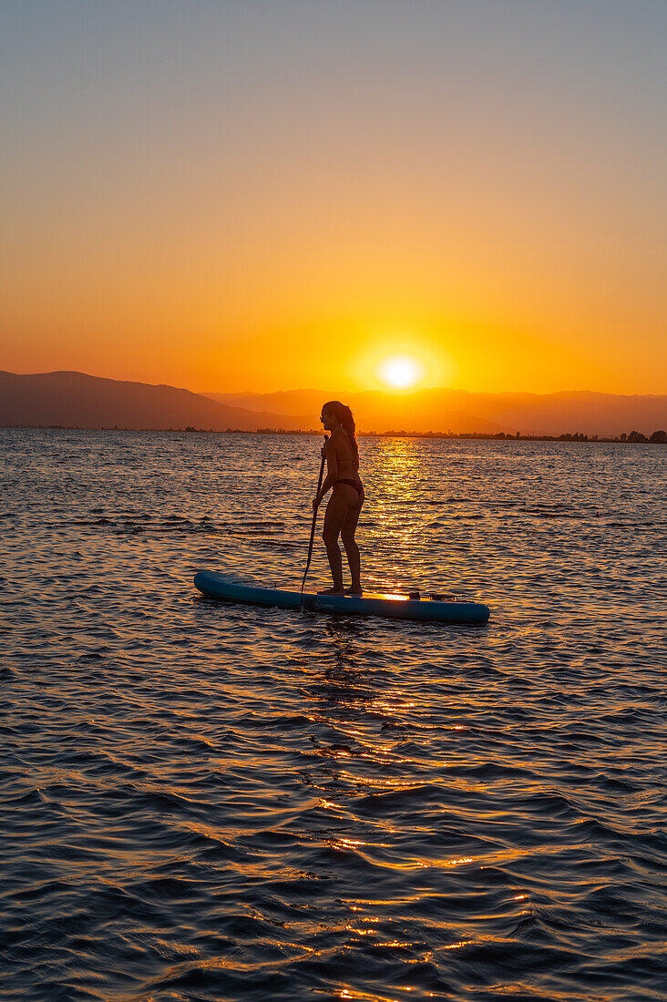 Silhouette of young woman practicing paddle surf during sunset at Trabucador beach, Ebro Delta, Tarragona, Spain\n