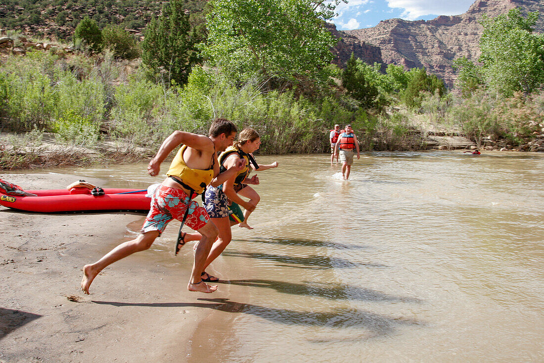 River guides running to jump in the water of the Green River on a rafting trip through Desolation Canyon in Utah.\n