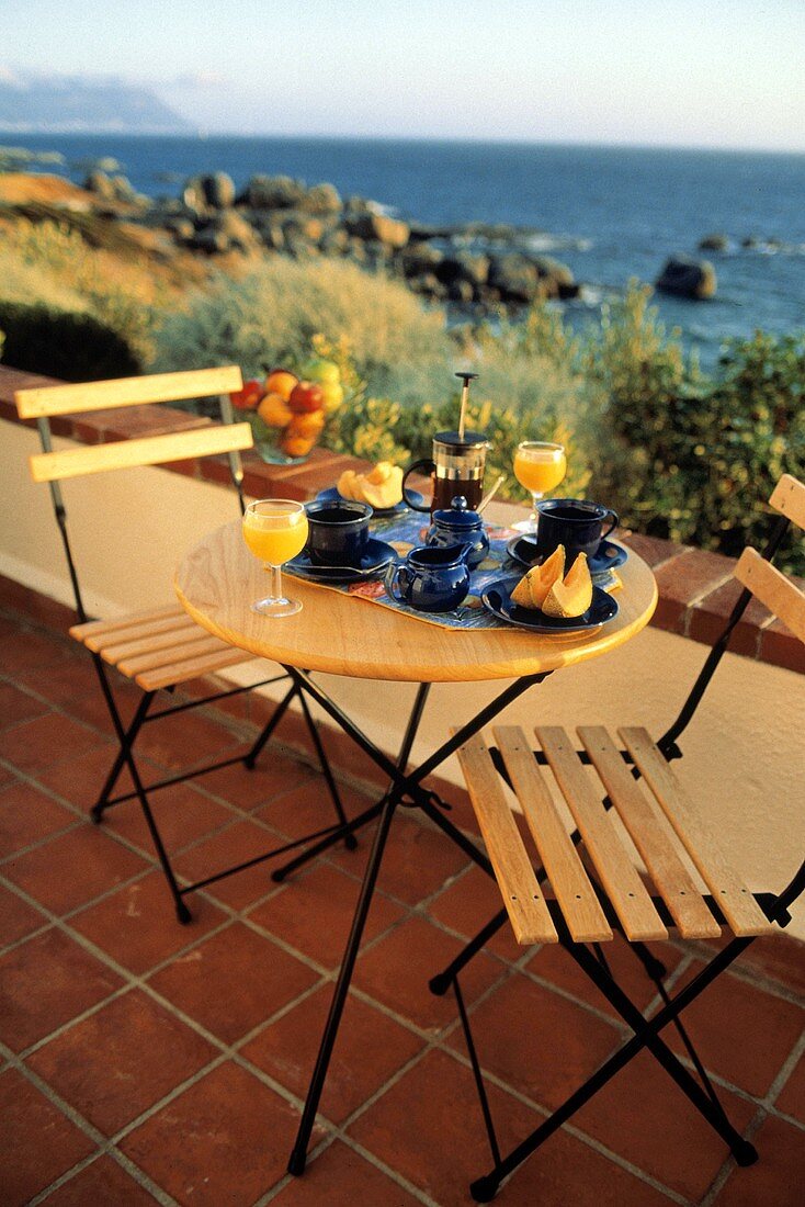 Frühstückstisch mit Kaffee,O-Saft,Melone auf Terrasse am Meer