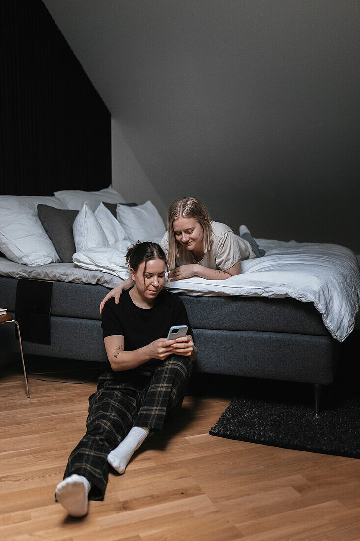 Homosexuelles weibliches Paar sitzt auf dem Bett und schaut auf das Handy