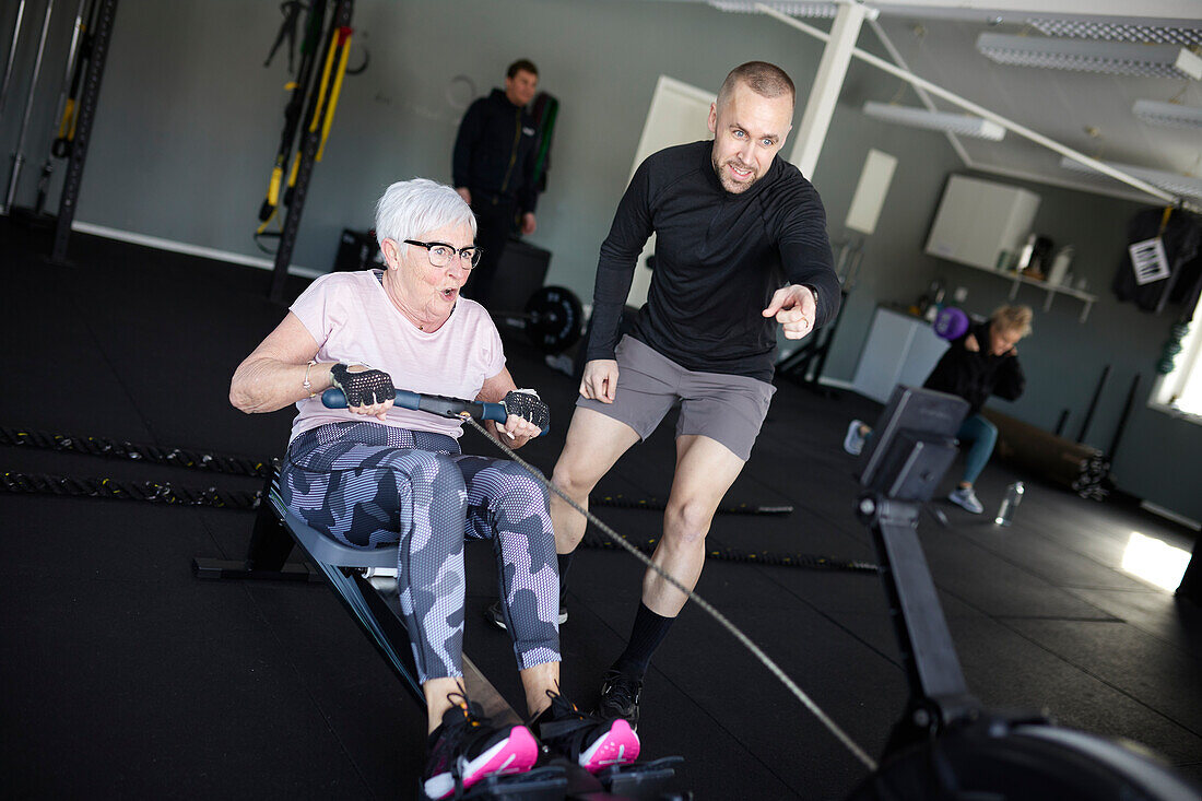 Coach assisting to senior woman exercising in gym\n