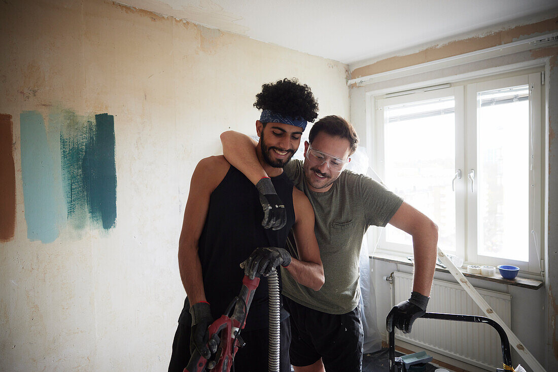 Lächelndes männliches homosexuelles Paar bei der Wohnungsrenovierung zusammenstehend