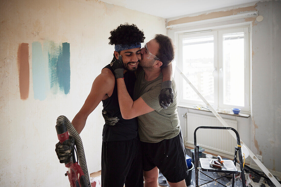 Männliches homosexuelles Paar küsst sich bei der Renovierung seiner Wohnung
