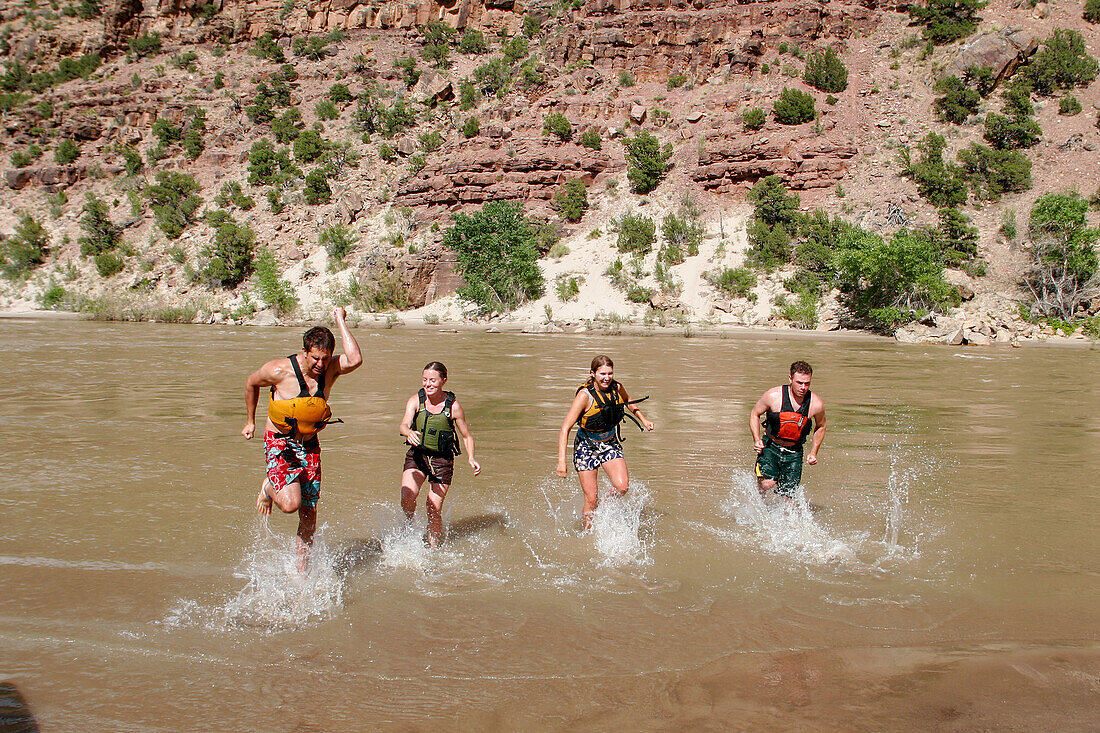 River guides running backward to jump in the water of the Green River on a rafting trip through Desolation Canyon in Utah.\n