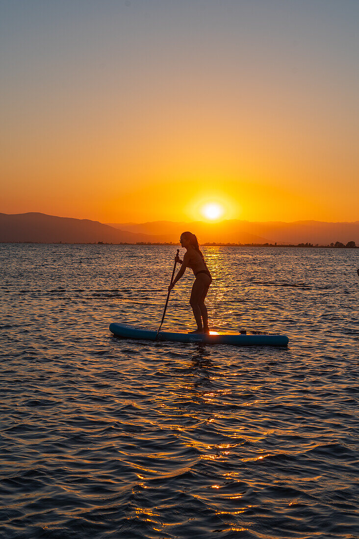 Silhouette of young woman practicing paddle surf during sunset at Trabucador beach, Ebro Delta, Tarragona, Spain\n
