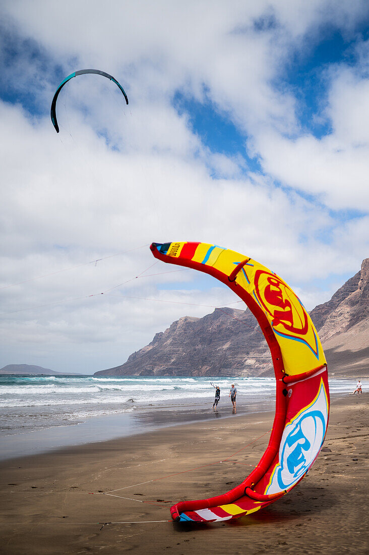Kite-Surfer am Strand von Famara (Playa de Famara), einem 6 km langen goldenen Sandstrand im Naturpark des Chinijo-Archipels, zwischen dem Fischerdorf La Caleta de Famara und dem Fuß der beeindruckenden Klippen von Famara, Lanzarote, Kanarische Inseln, Spanien