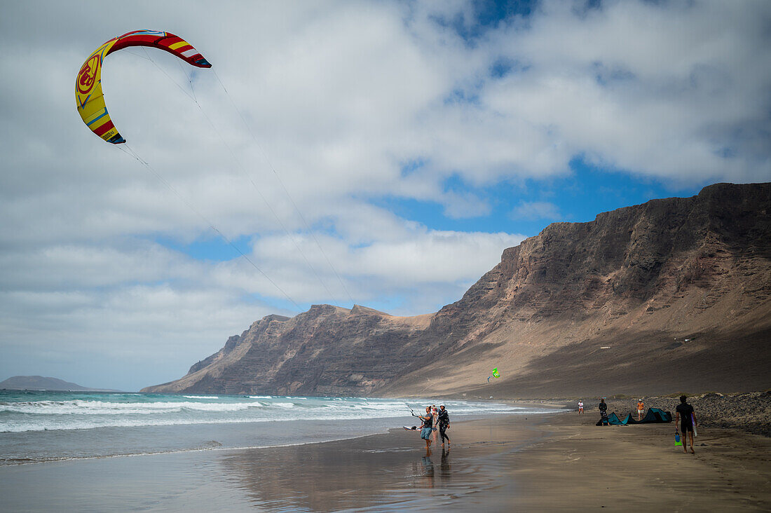 Kite surfers in Famara beach (Playa de Famara), 6km golden sand beach located within the Natural Park of the Chinijo Archipelago, between the fishing village of La Caleta de Famara and the base of the impressive cliffs of Famara, Lanzarote, Canary Islands, Spain\n