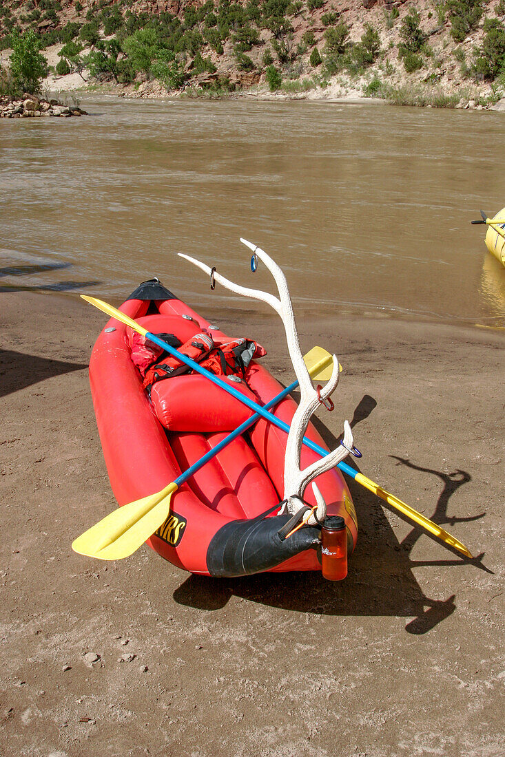 A duckie or inflatable kayak with an elk antler attached on the shore in Desolation Canyon, Utah.\n