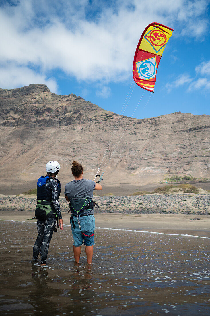 Kite-Surfer am Strand von Famara (Playa de Famara), einem 6 km langen goldenen Sandstrand im Naturpark des Chinijo-Archipels, zwischen dem Fischerdorf La Caleta de Famara und dem Fuß der beeindruckenden Klippen von Famara, Lanzarote, Kanarische Inseln, Spanien