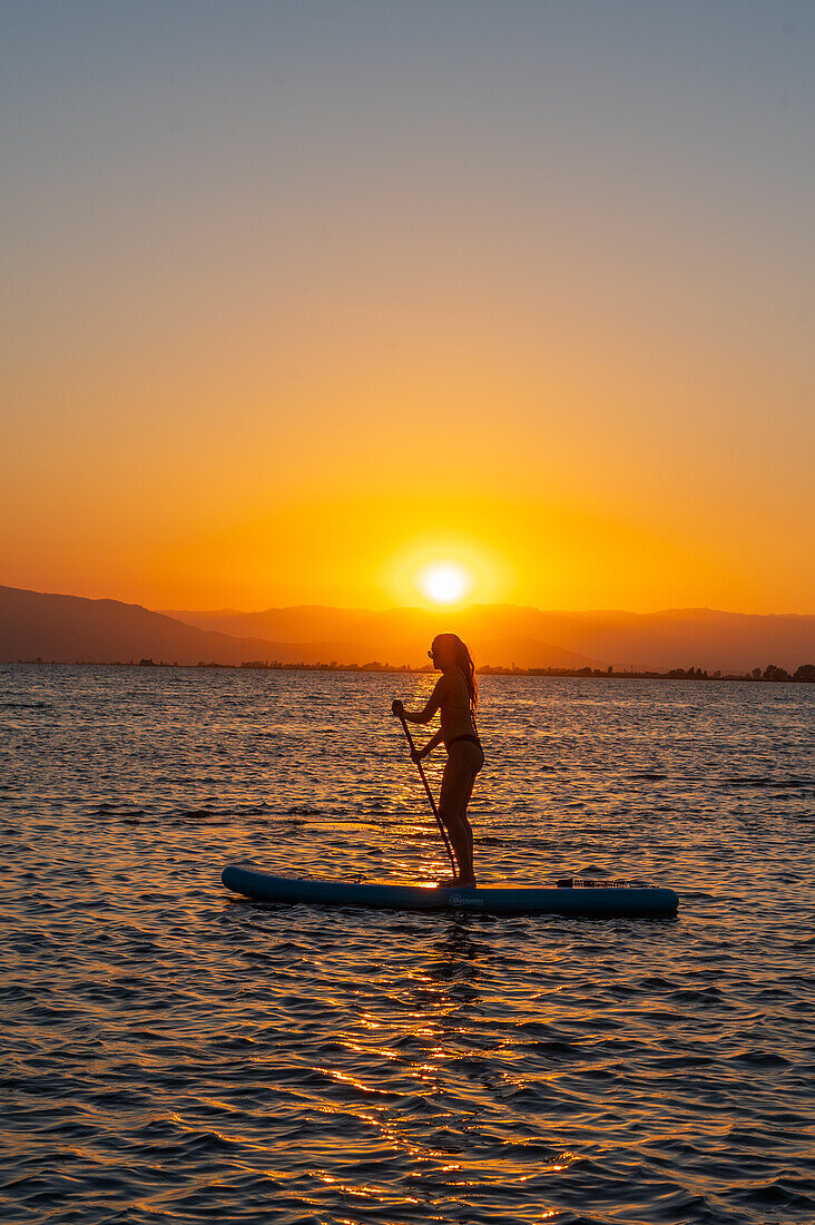 Silhouette of young woman practicing paddle surf during sunset at Trabucador beach, Ebro Delta, Tarragona, Spain\n