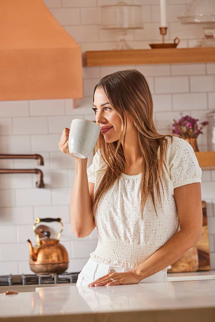 Woman drinking from mug in kitchen\n