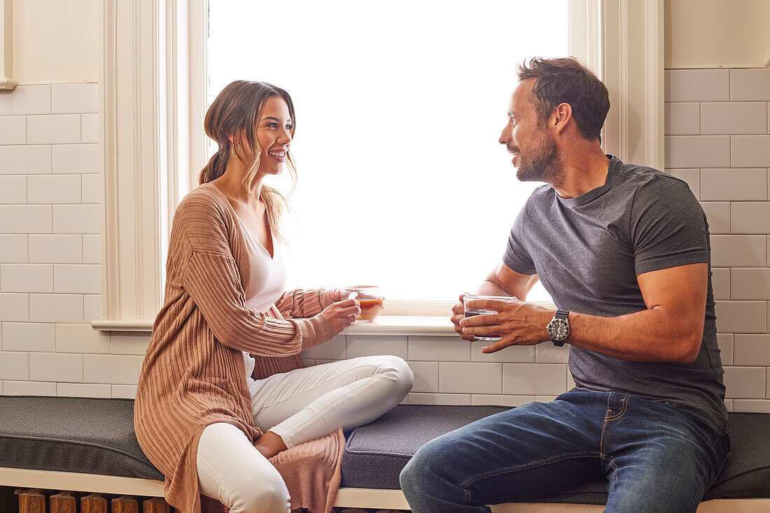 Smiling couple relaxing by window at home\n