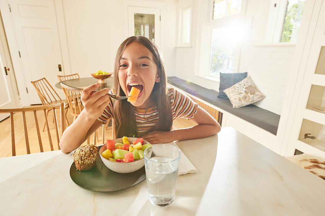 Smiling girl (12-13) having breakfast in kitchen\n