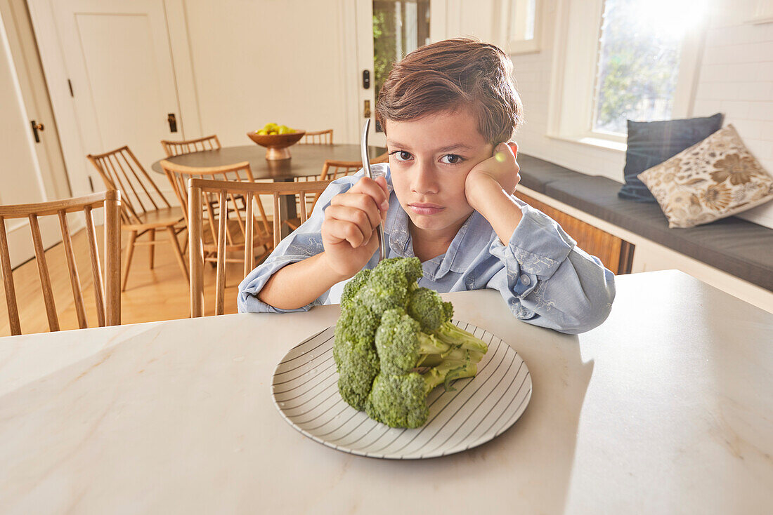 Unzufriedener Junge (8-9) schaut auf Brokkoli auf dem Teller in der Küche