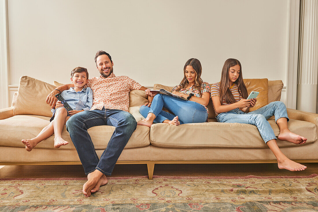 Smiling family with two children (8-9, 12-13) relaxing on sofa\n