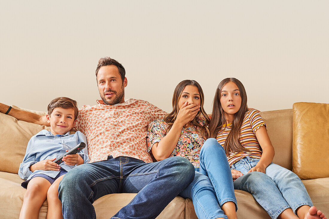 Familie mit zwei Kindern (8-9, 12-13) beim Fernsehen auf dem Sofa