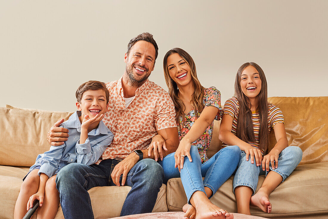 Porträt einer lächelnden Familie mit zwei Kindern (8-9, 12-13), die auf dem Sofa fernsehen