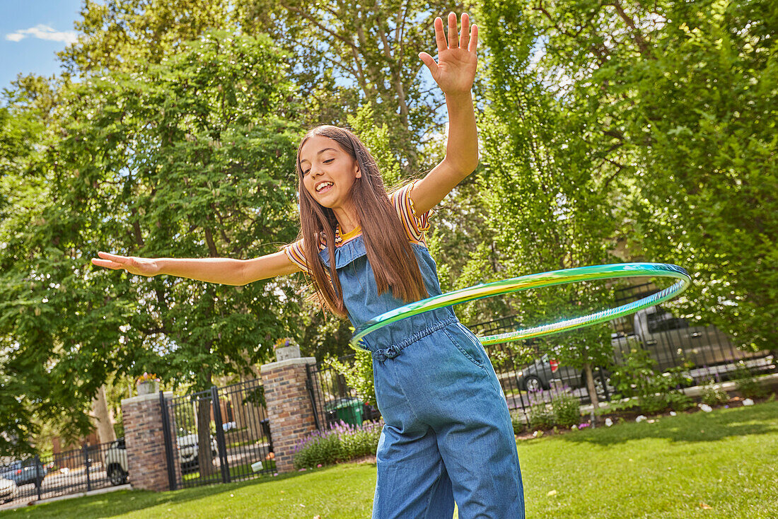 Smiling girl (12-13) playing with hula hoop in park\n