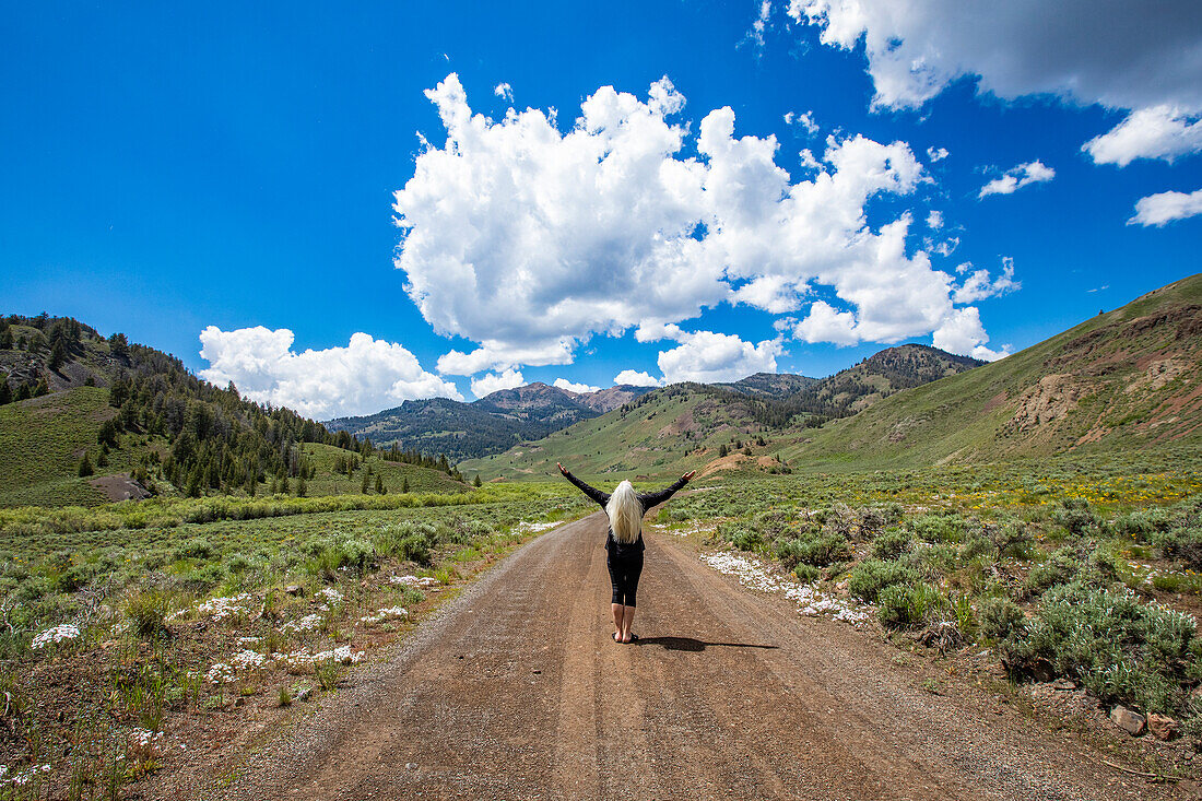 USA, Idaho, Sun Valley, Rear view of senior woman standing with arms raised on road and looking at mountains\n