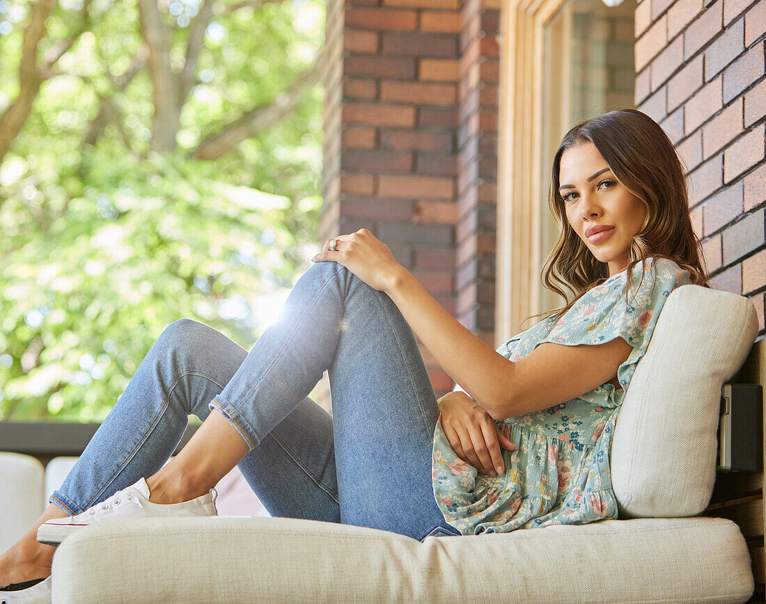 Porträt einer Frau mittleren Alters, die sich auf dem Sofa auf der Terrasse entspannt