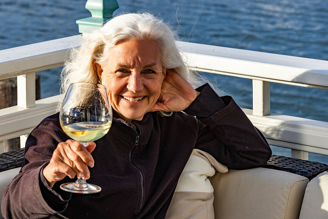 Portrait einer lächelnden älteren Frau, die sich mit einem Glas Wein entspannt