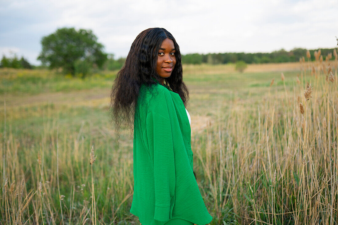 Brunette woman wearing green blouse and standing in field \n