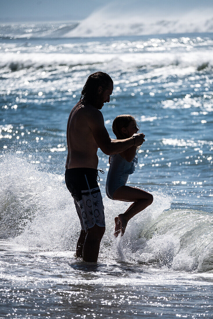 Father playing on the beach with son.\n