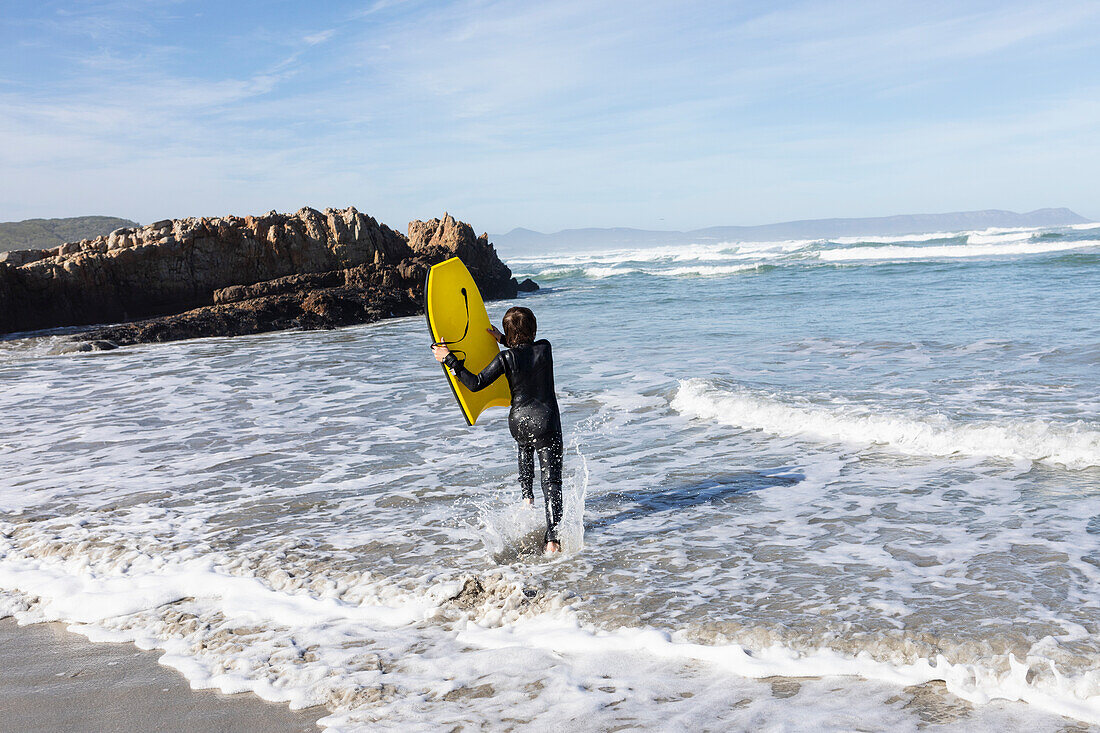 South Africa, Hermanus, Boy (10-11) entering Atlantic Ocean with body board in Kammabaai Beach\n