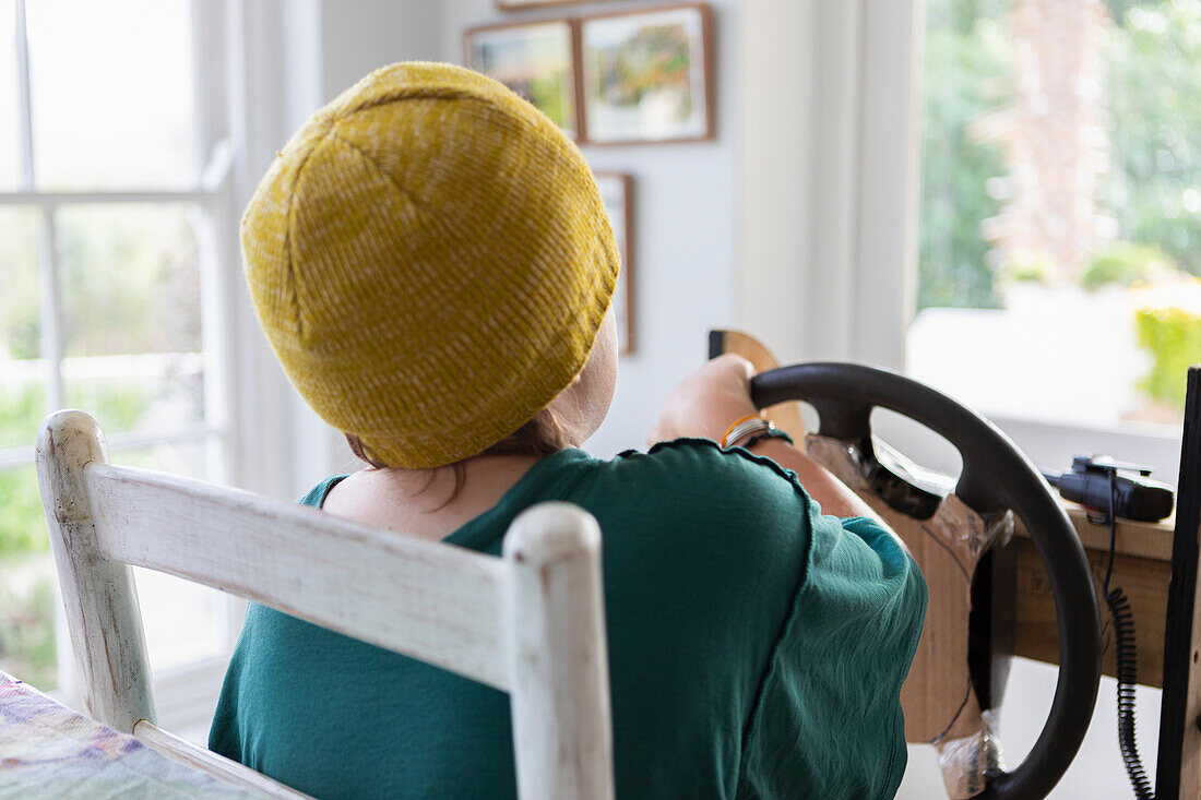 Rear view of boy (10-11) pretending to drive homemade steering wheel at home\n