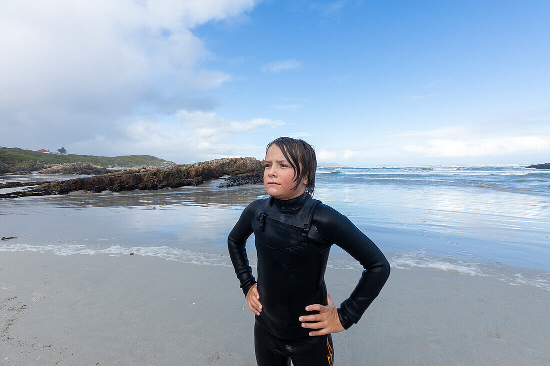 Portrait of young surfer (10-11) standing by Atlantic Ocean in Kammabaai Beach\n