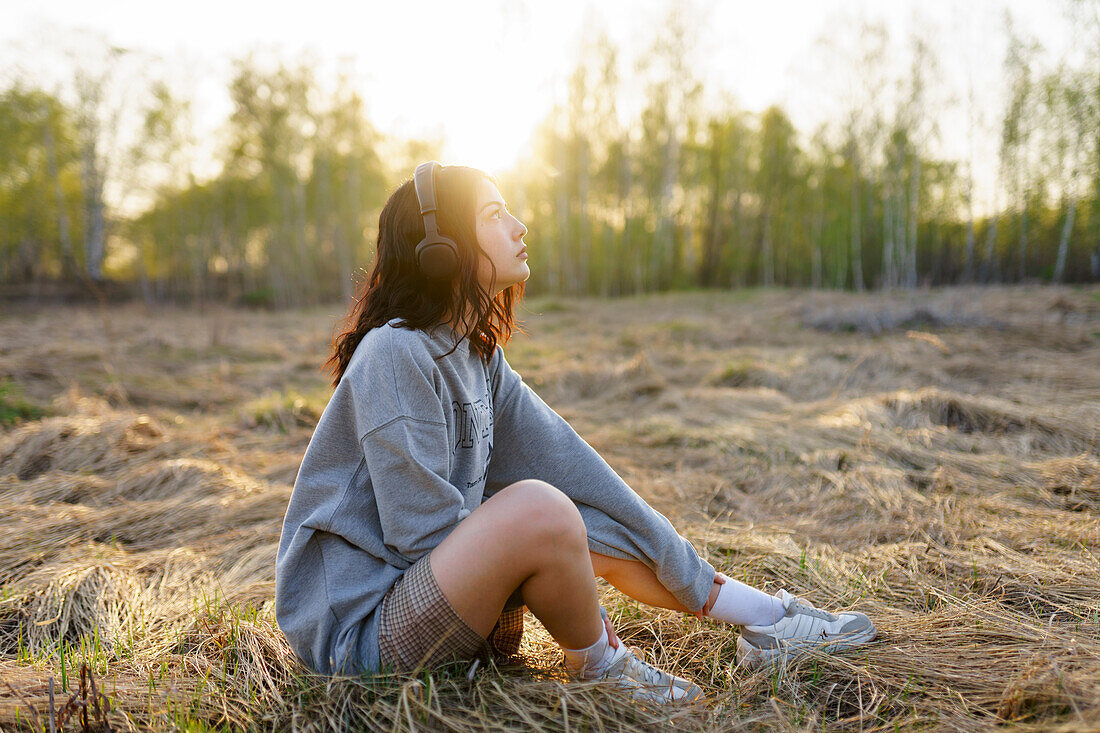 Seitenansicht einer Frau, die Musik hört, während sie auf einer Wiese bei Sonnenuntergang sitzt