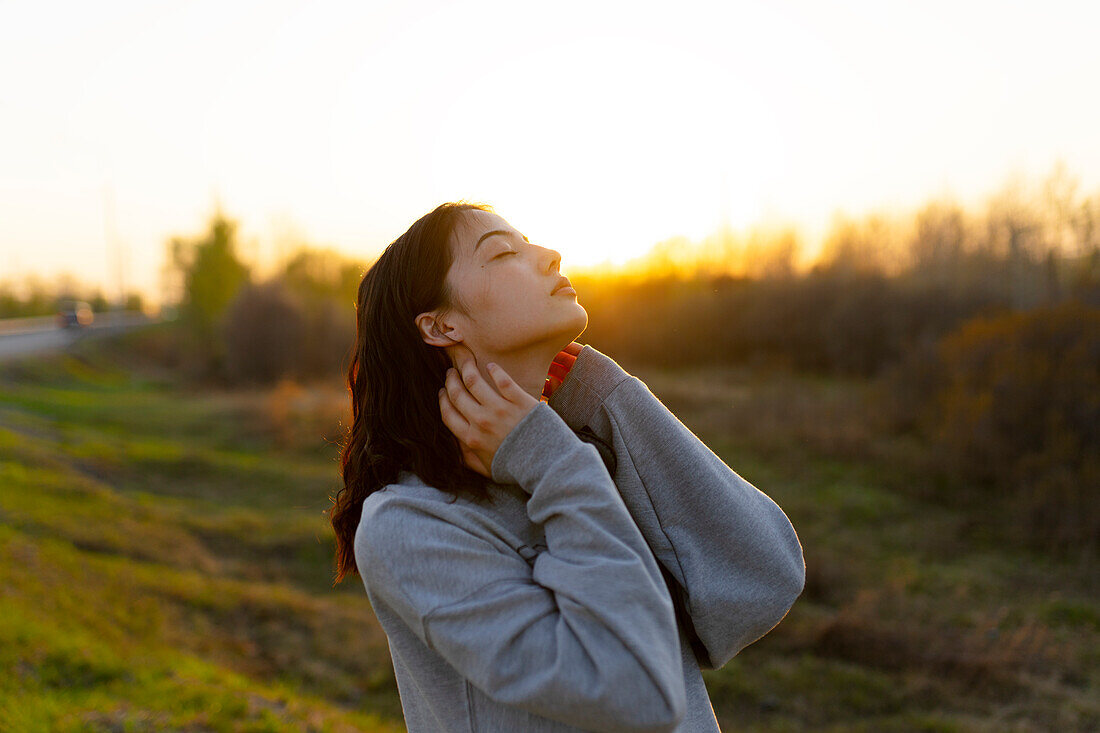 Portrait einer nachdenklichen Frau mit geschlossenen Augen auf einer Wiese bei Sonnenuntergang