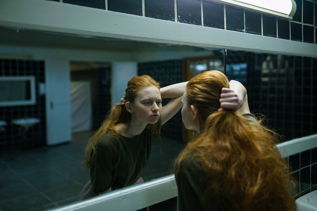 Young woman looking in mirror in public bathroom\n