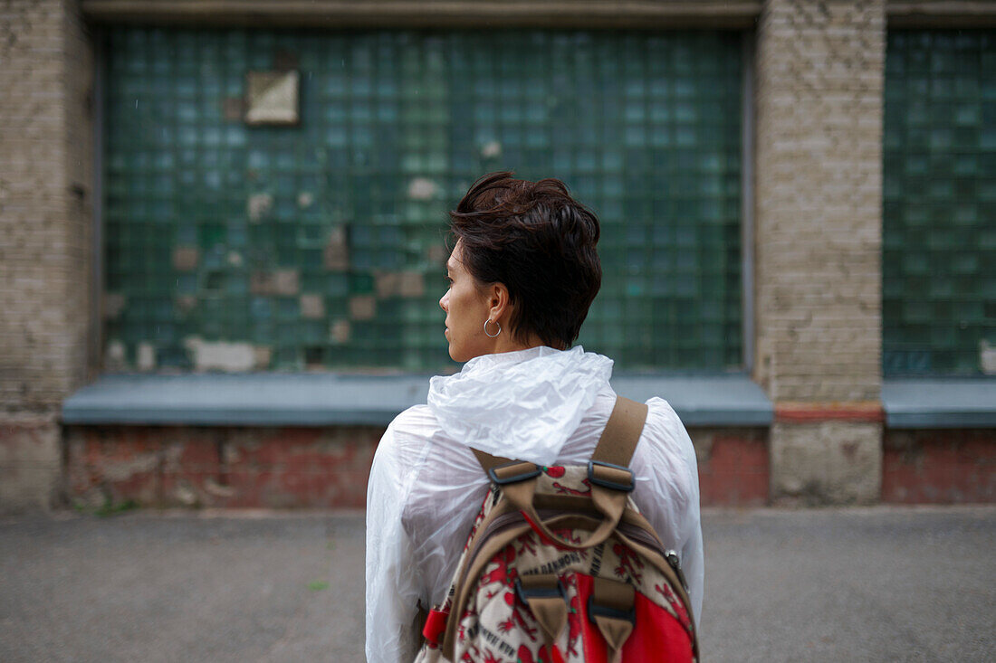 Rückansicht einer jungen Frau, die mit Rucksack in der Stadt steht und wegschaut