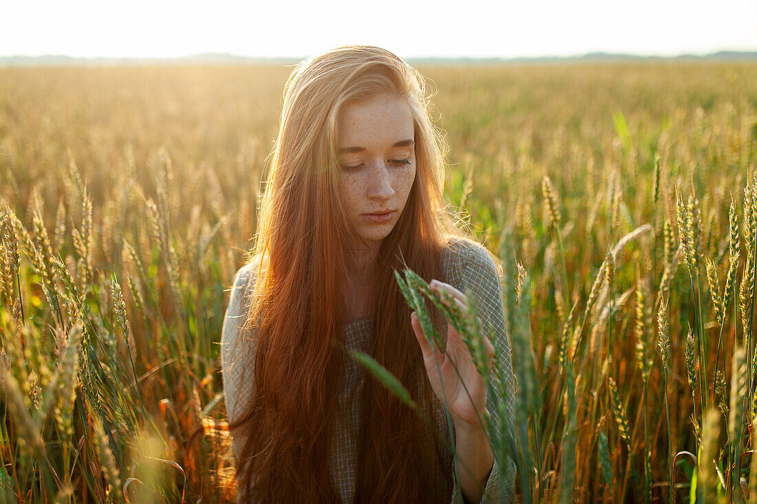 Portrait of young woman looking at cereal plants in field\n