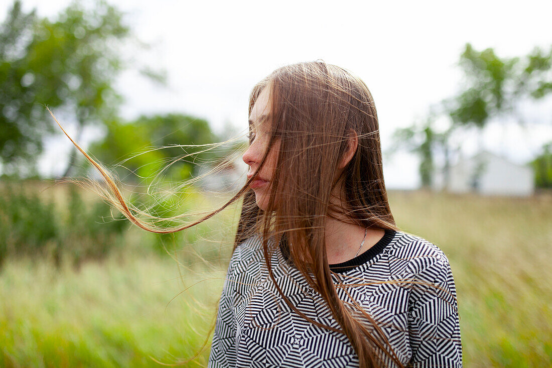 Blonde young woman with tousled hair in field \n