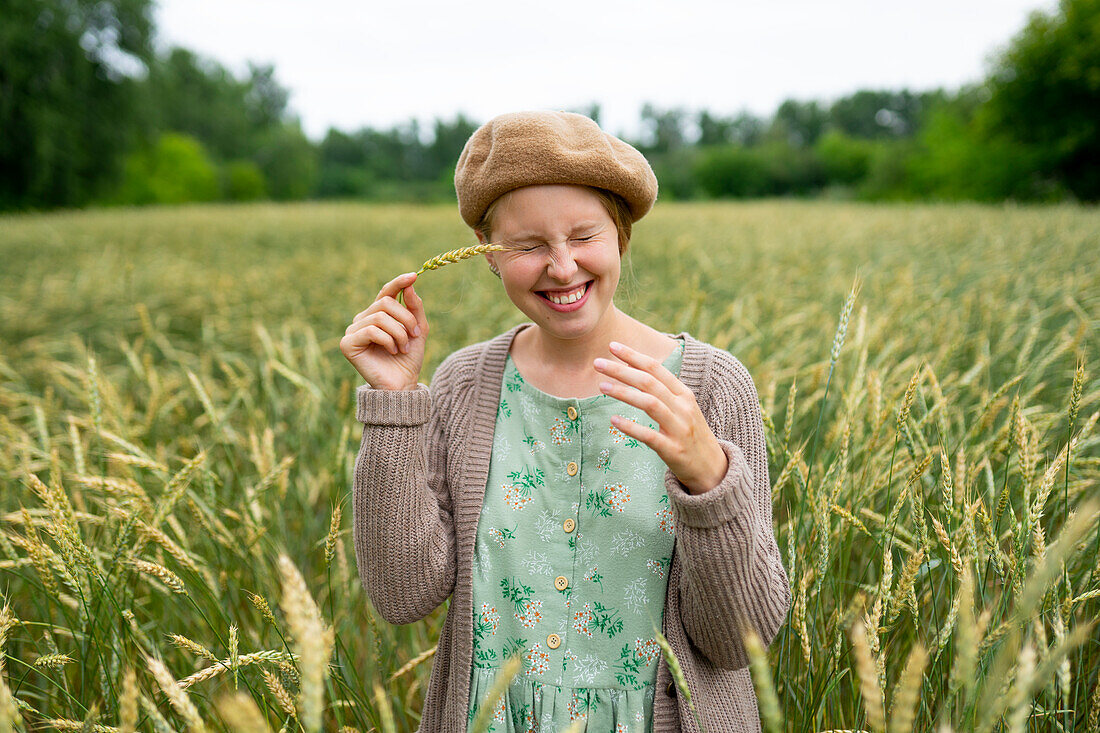 Smiling woman with closed eyes touching face with ear of wheat \n