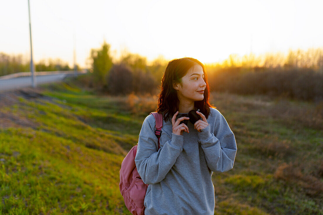 Frau mit Kopfhörern und Rucksack, wegschauend bei Sonnenuntergang