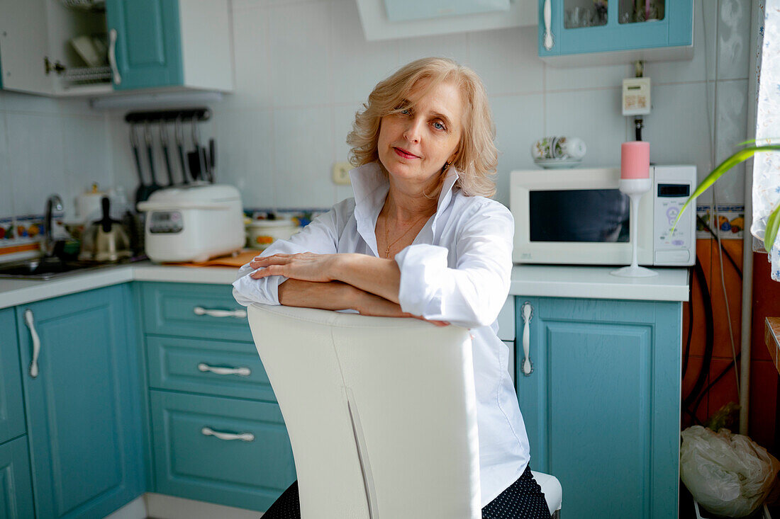 Woman sitting on chair in kitchen, looking at camera \n