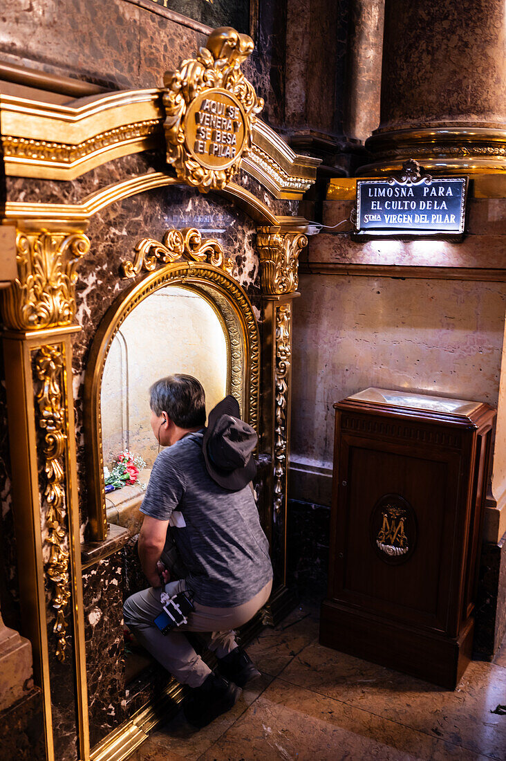 Asian worshipers kissing the pillar inside the Cathedral-Basilica of Our Lady of the Pillar during The Offering of Flowers to the Virgen del Pilar, the most important and popular event of the Fiestas del Pilar held on Hispanic Day, Zaragoza, Spain\n