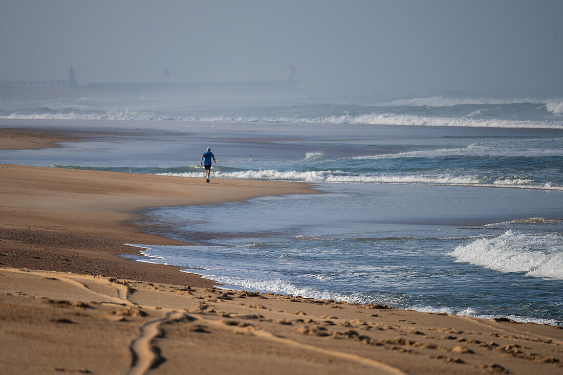 Mann, der an einem leeren Strand von Les Culs Nus in Hossegor, Landes, Frankreich, spazieren geht.