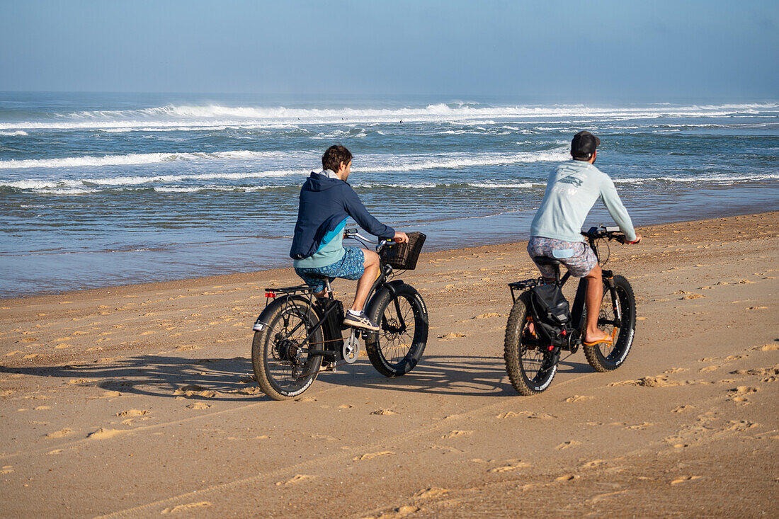 Two young men riding their bikes on the sand during Quiksilver Festival celebrated in Capbreton, Hossegor and Seignosse, with 20 of the best surfers in the world hand-picked by Jeremy Flores to compete in south west of France.\n