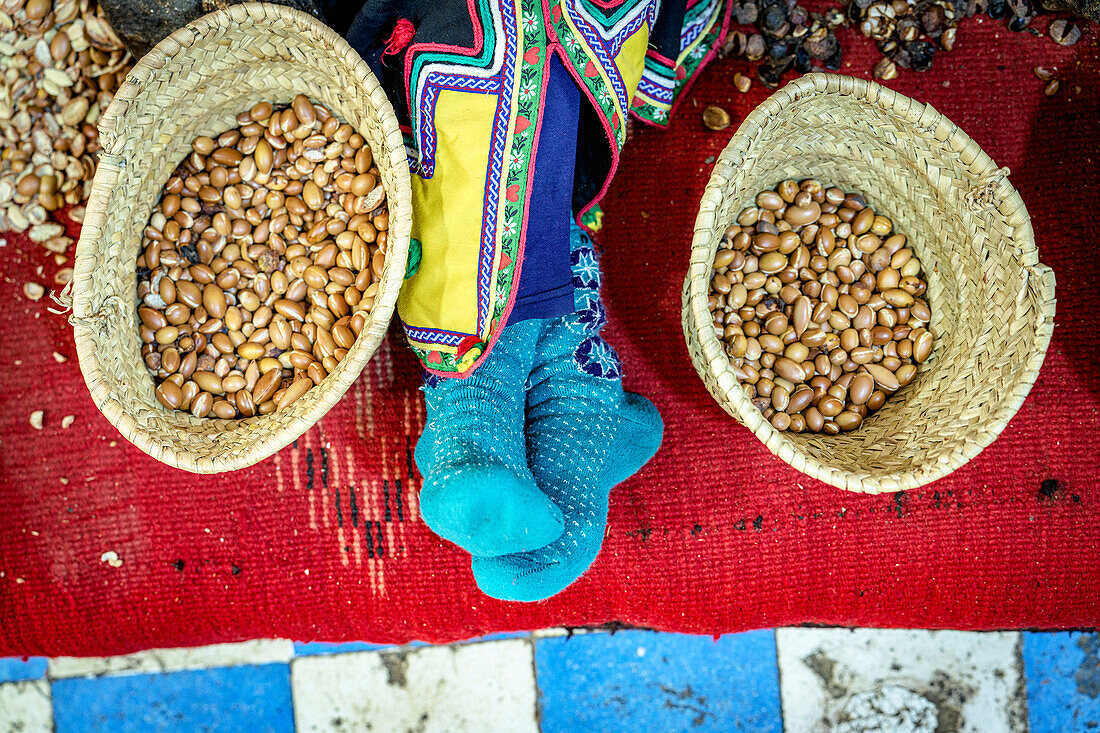 Hochformatige Ansicht eines Arbeiters, der sich neben Strohkörben voller Samen für die Herstellung von Arganöl ausruht, Marokko, Nordafrika, Afrika