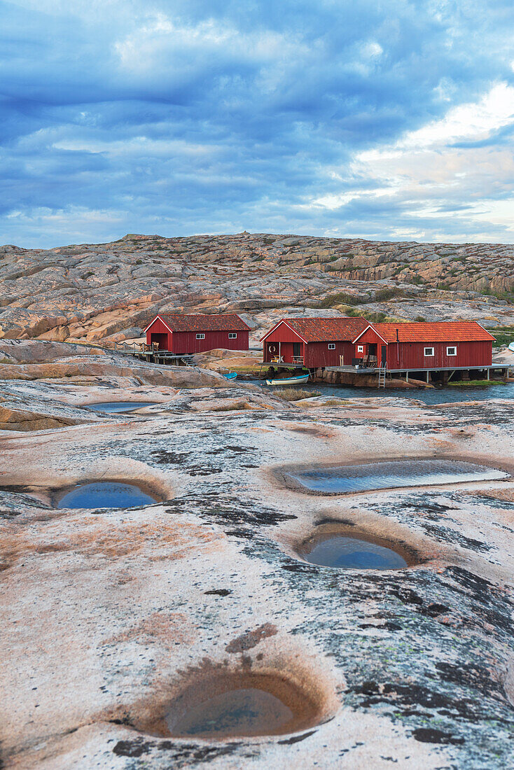 Red traditional wooden cottages on granite rock in a cloudy day, Ramsvik island, Bohuslan, Vastra Gotaland, Sweden, Scandinavia, Europe\n