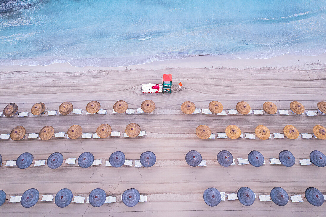 Luftaufnahme von Reihen von Sonnenschirmen mit einem Rettungsschwimmerturm an einem Sandstrand, Insel Sizilien, Italien, Mittelmeer, Europa