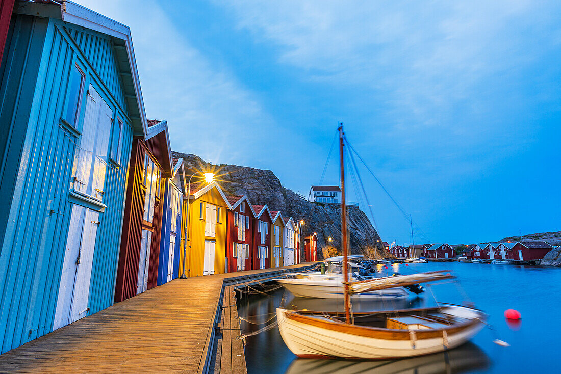 Bunte Fischerhütten mit Holzboot am Steg in der Abenddämmerung, Smogen, Bohuslan, Vastra Gotaland, Westschweden, Schweden, Skandinavien, Europa