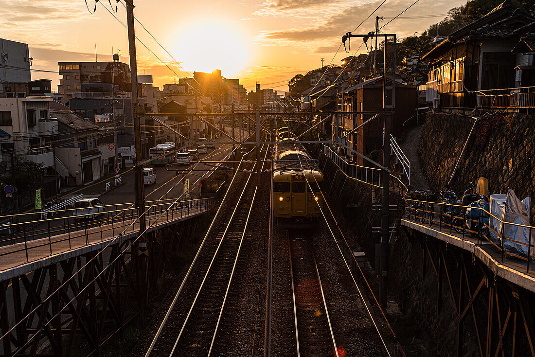 View from a railway bridge with a yellow Japanese train approaching during sunset, Onomichi, Honshu, Japan, Asia\n