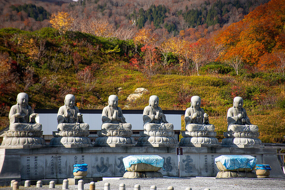 Row of six shizo statues with a beautiful autumnal landscape in the background, Osorezan Bodaiji Temple, Mutsu, Aomori prefecture, Honshu, Japan, Asia\n