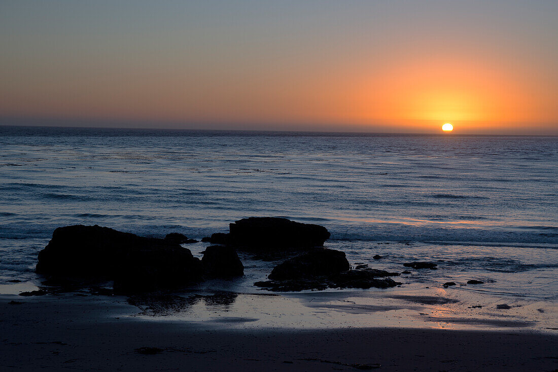 Sunset over the ocean, with rocks in the foreground, San Simeon, California, United States of America, North America\n