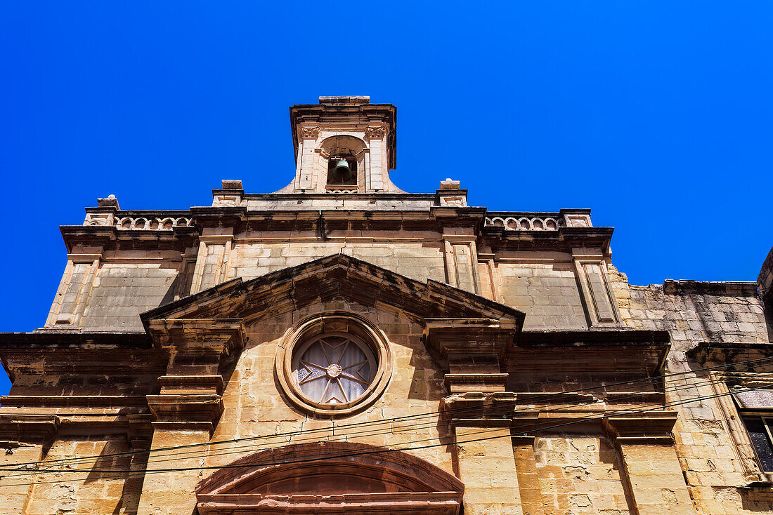 Malta Oratory of The Holy Cross exterior with limestone, Maltese cross and bell tower under a bright blue sky, old city of Birgu (Citta Vittoriosa), Malta, Mediterranean, Europe\n